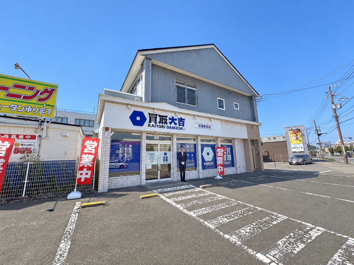 室蘭駅前店の外観、入口に立つ店長と店舗前の無料駐車場